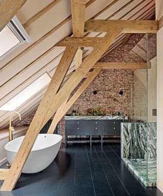 bathroom with vaulted ceiling, exposed brick wall, freestanding tub, gray double washstand, gray painted floorboards and marble shower splashback