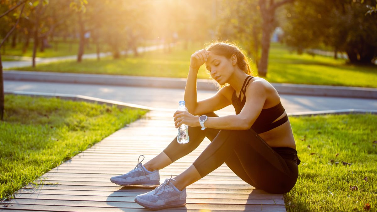 sporty woman resting and hydrating with water after running outdoors and looking very tired