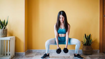 A woman performing a squat with dumbbells as part of a leg workout 