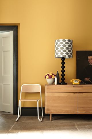 mustard wall with a wooden sideboard and a monochrome patterned lampshade