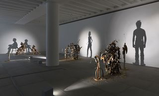 Closer view of the ’Nihilistic Optimistic’ exhibition. Shadow sculptures made out of junk, metal, and wood are placed throughout the area. The light shines on the sculptures and casts shadows on the walls. The shadows portray both artists.