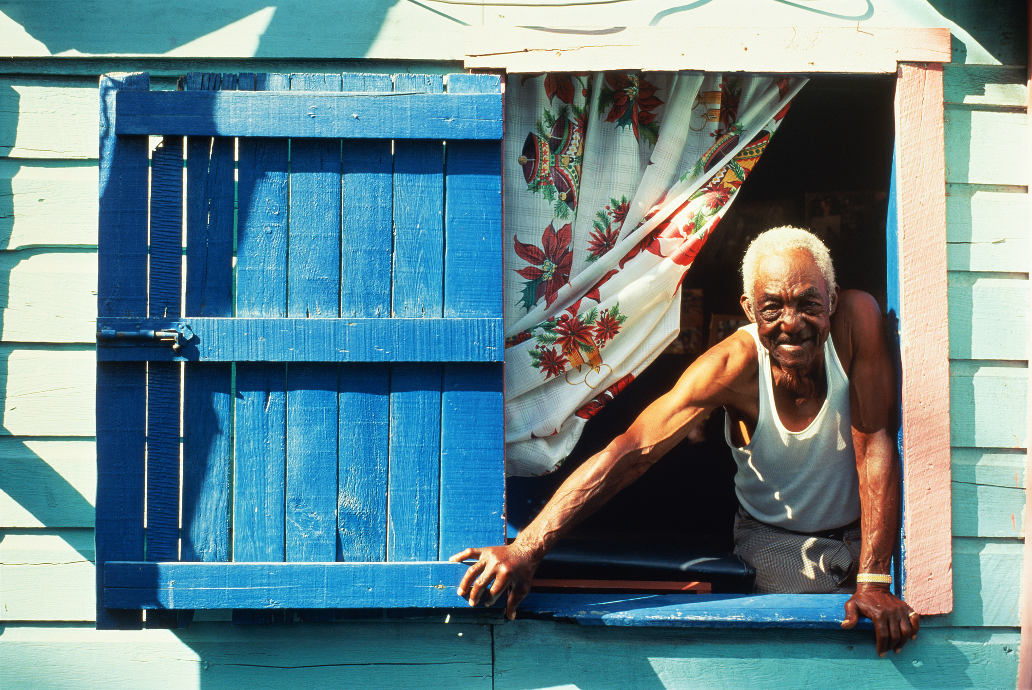 An older Creole man leans out of a window, smiling, in Belize.