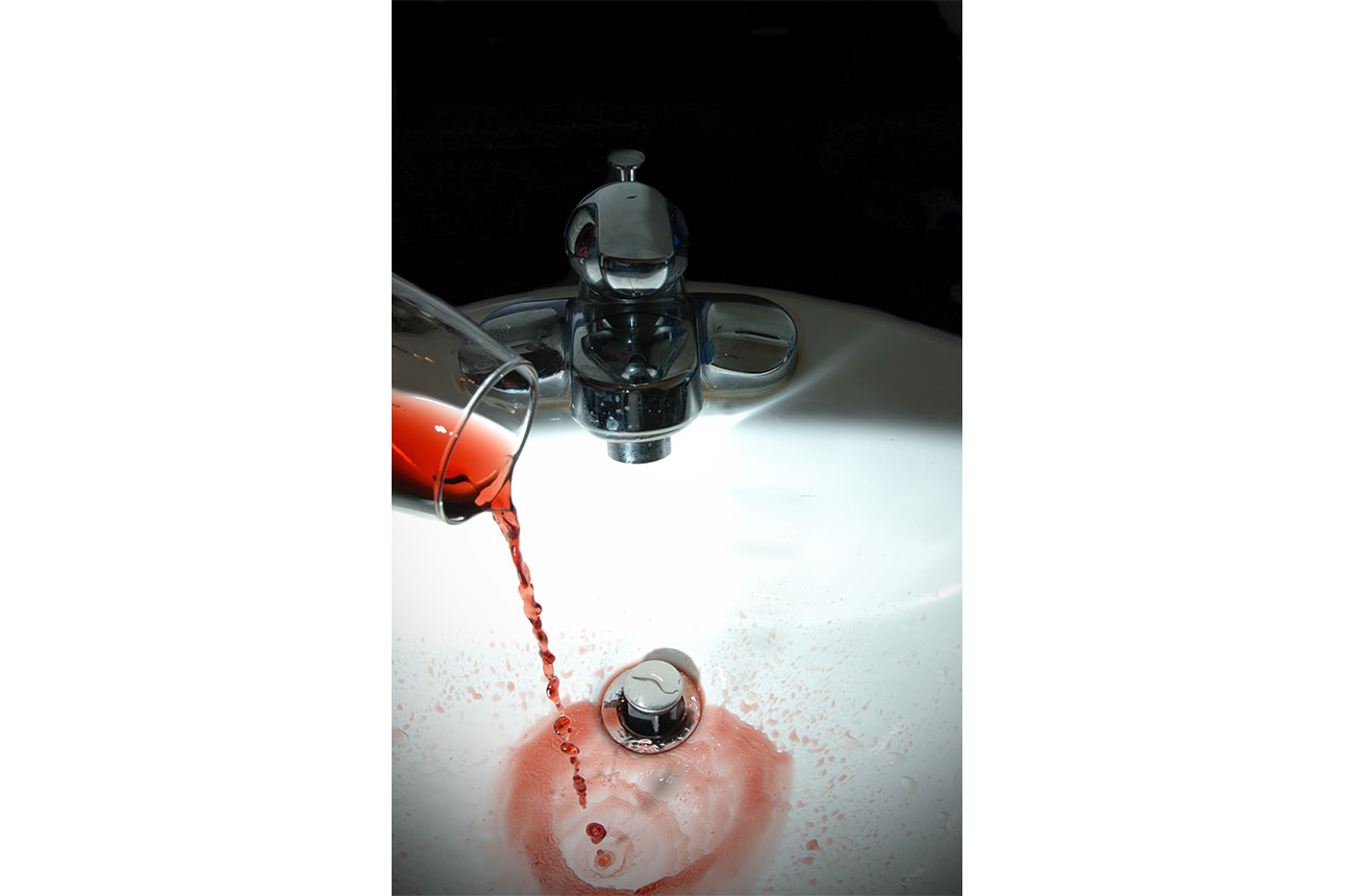 Bottle of red wine being poured down sink