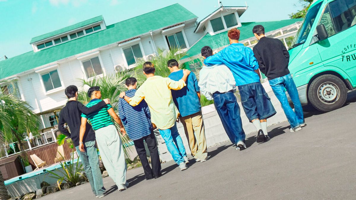 A group of people stand with their backs to the camera all arm in arm 