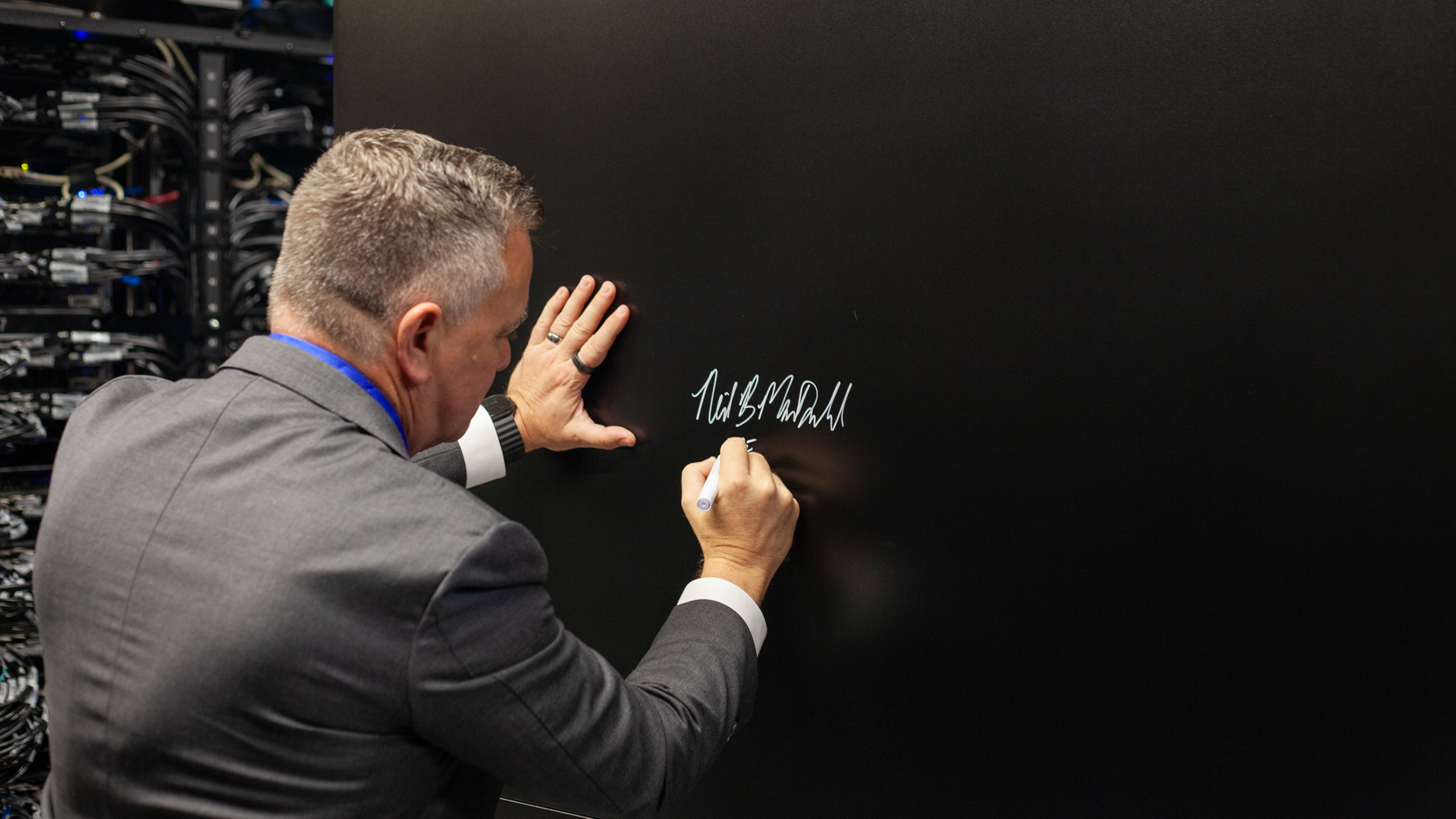 Neil MacDonald, EVP & GM, HPE Server Business, signing the Isambard-AI supercomputer at its official inauguration. MacDonald is signing the side of a server cabinet with a white sharpie, with his back to the camera.