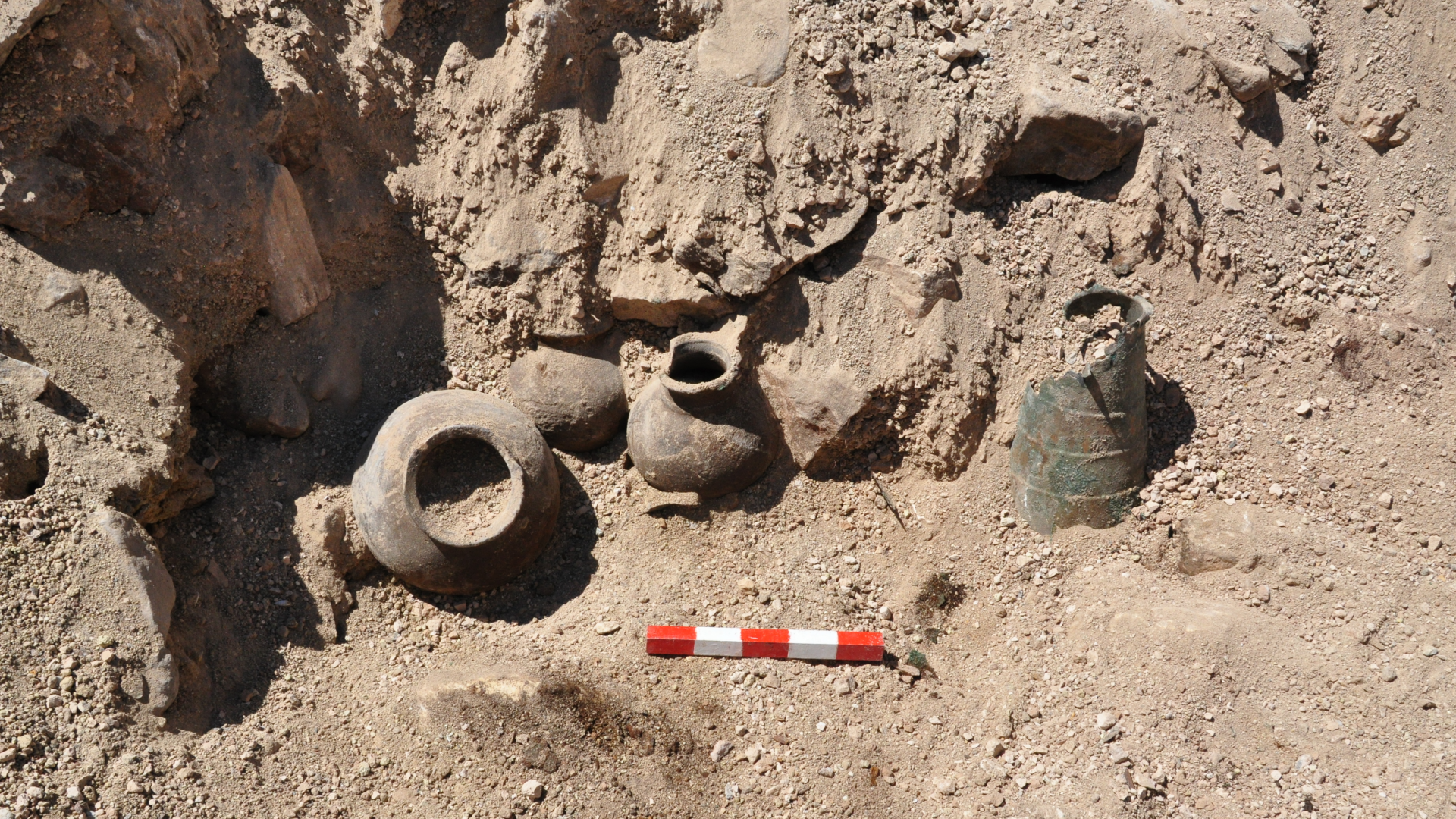 several ceramic jars and a bronze pot being excavated on an archaeological site