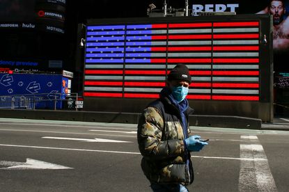 A man wears a face mask as he check his phone in Times Square on March 22, 2020 in New York City. - Coronavirus deaths soared across the United States and Europe on despite heightened restric