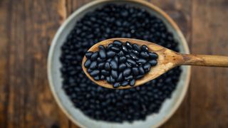 Black beans, raw, on wooden spoon over bowl of black beans