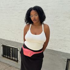 a woman wearing a white tank top, pink utility belt, and black skirt