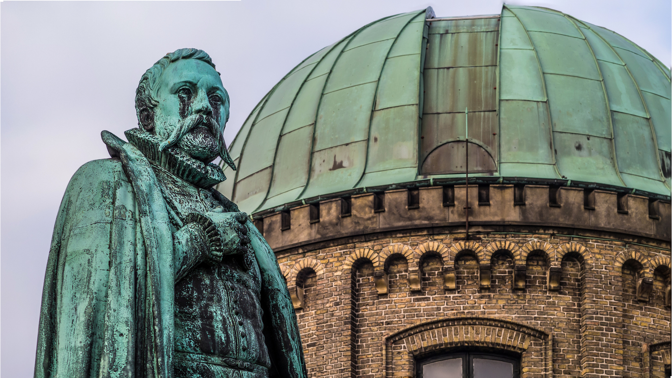 Statue of Tycho Brahe in front of a green copper roofed observatory next to Rosenborg castle in Copenhagen, Denmark.