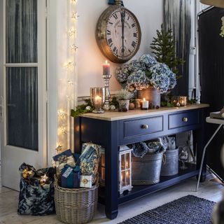 Blue console with Christmas decorations and presents below bronze wall clock