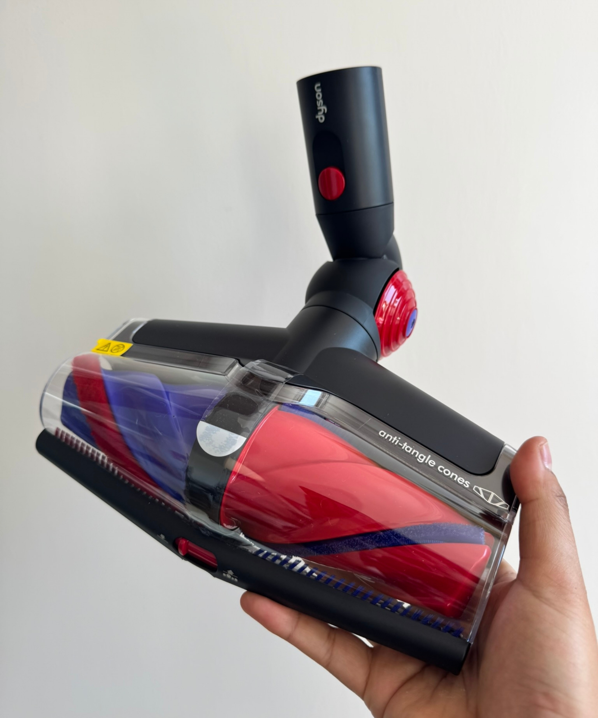 Dyson V16 Piston Animal's red and blue floorhead being held in front of white wall.