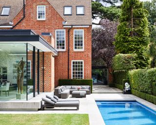 A swimming pool with a patio and seating area next to a large country house