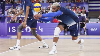 Earvin Ngapeth, in blue shirt and shorts, digs the ball out of trouble for France in the men's volleyball at the 2024 Paris Olympic Games.