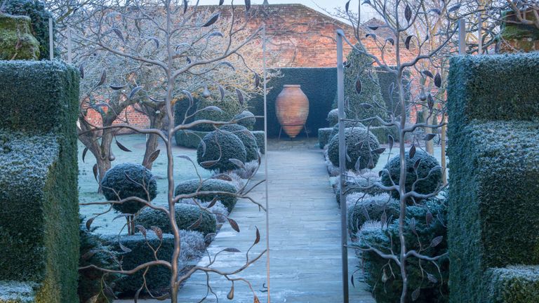 Winter garden with frosted handcrafted metal gates, box hedges and topiary