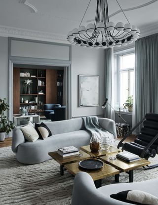 light gray living room with two gray sofas facing each other, a square gold coffee table, chandelier overhead, and a doorway leading through to another living room