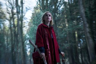 KIERNAN SHIPKA walks in a red cloak through the woods in a still from the chilling adventures of sabrina