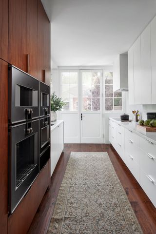 galley kitchen with walnut cabinets and white cabinets with double ovens and oriental rug on dark wood flooring