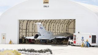 a white jet sits in a hangar in the desert