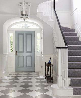 Gay and white checkered floor tiles and a sweeping white staircase.