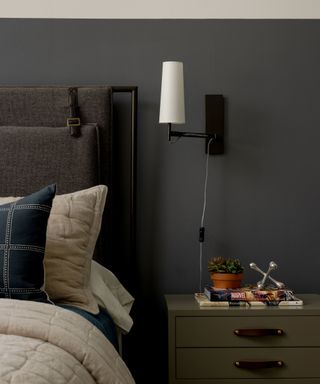 corner of bedroom with dark gray wall, olive green nightstand, neutral bedding