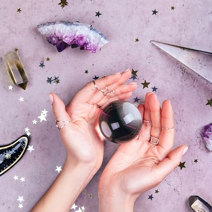  New Year's resolutions: Hands with rings on fingers are holding crystal ball near esoteric set on concrete gray background with many stars sequins