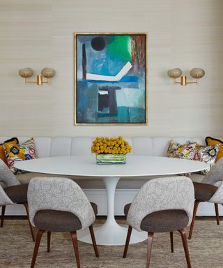 dining area with round white table and chairs, patterned cushions and blue abstract artwork