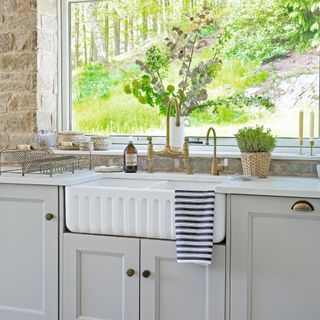 white kitchen sink with neutral cabinets underneath windows