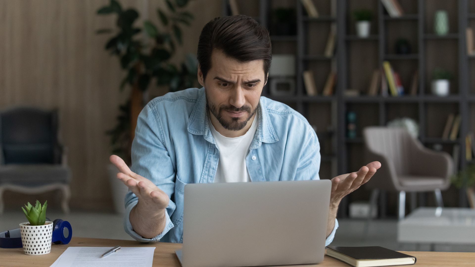 Seorang pria mengerutkan kening dan menunjuk laptopnya dengan sikap frustrasi