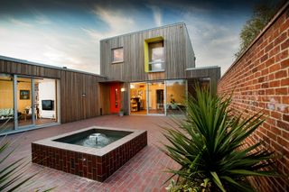 A timber clad house with a paved courtyard and a water feature