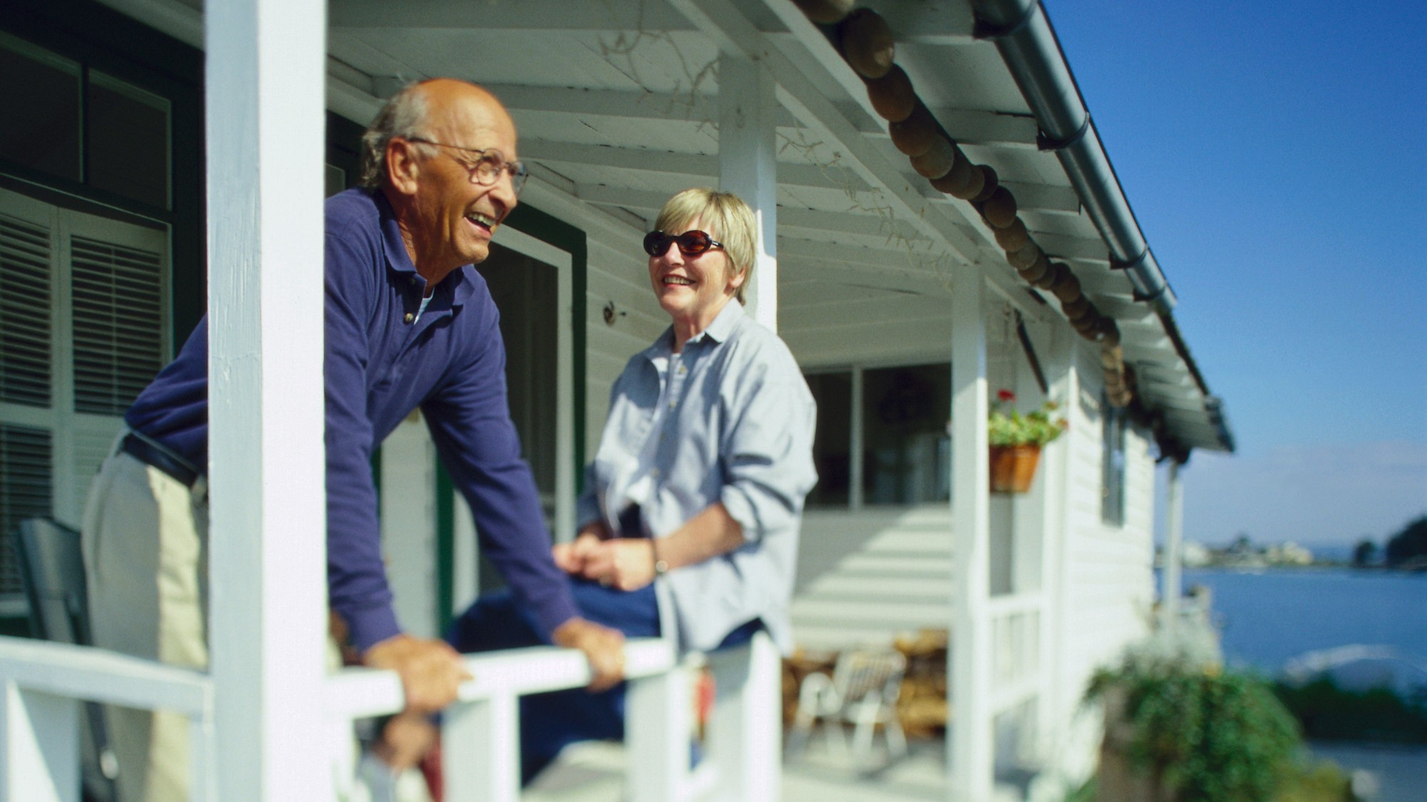 An older couple relaxes on the porch of a beach house.
