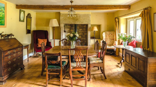 17th century farmhouse dining room featuring a wooden table and chairs, hardwood floors and a stone fireplace