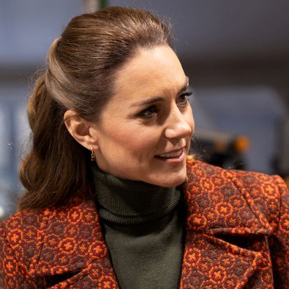Princess Kate wearing an orange coat and green turtleneck turning to the side and smiling