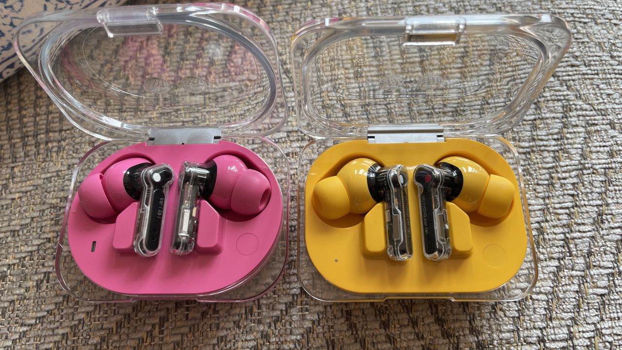 Nothing Ear (3a) in pink and Nothing Ear (a) in yellow, held in a hand and on beige background