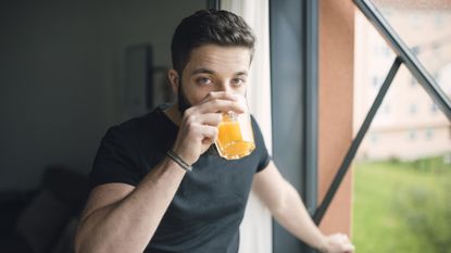 Man stands next to window drinking from glass and looks at the viewer