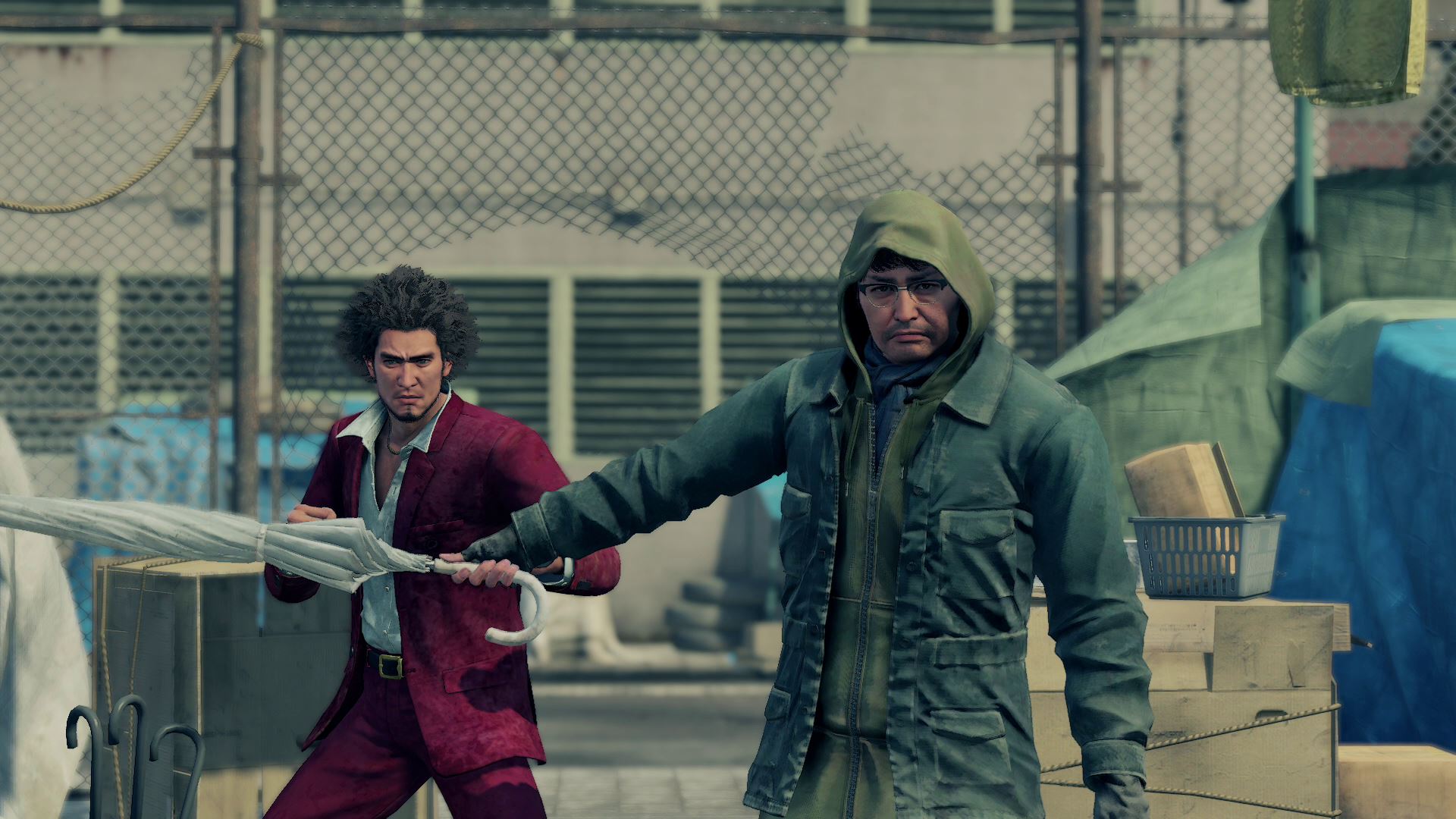 Yu Nanba stands in front of protagonist Ichi holding an umbrella in front of him as if to protect him in Yakuza: Like a Dragon