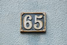 The number 65 on a number plate against a textured wall