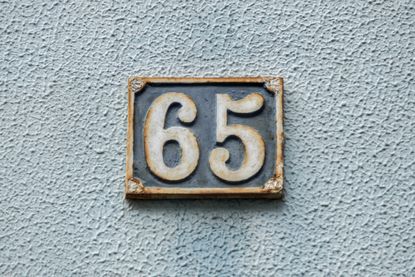 The number 65 on a number plate against a textured wall