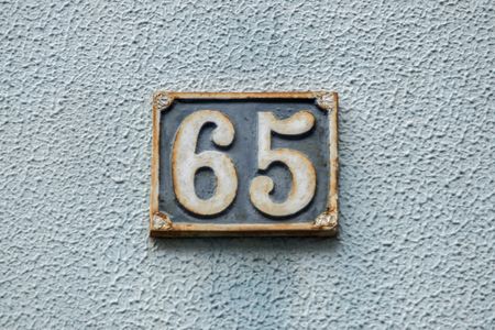 The number 65 on a number plate against a textured wall