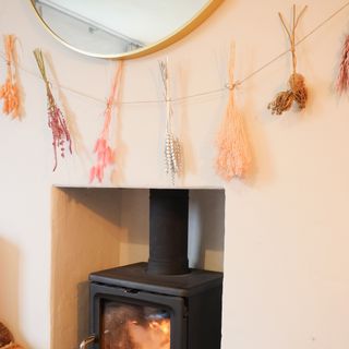 christmas flower arrangement of a dried flower garland hung up on a peach coloured wall above a woodburner fireplace