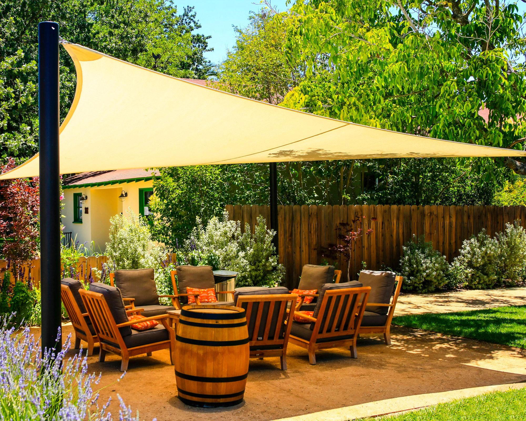 shade sail covering patio and garden furniture, in garden with fence, shrubs, lawn and trees