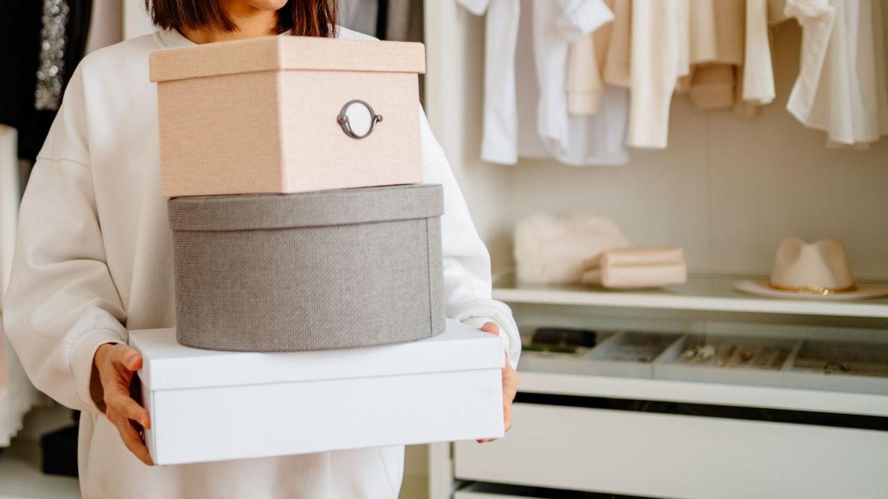 A soman with short brown hair carrying a stack of small boxes out of a walk in closet