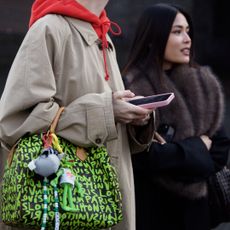 a guest at Copenhagen Fashion Week carries a louis vuitton bag with a trench coat and hoodie