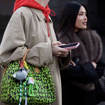 a guest at Copenhagen Fashion Week carries a louis vuitton bag with a trench coat and hoodie