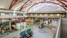 A photo of an airport terminal at Pittsburgh International Airport, taken with a wide angle lens to show off a high ceiling and the a good range of the interior. The terminal is largely empty.
