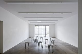 A gallery space at Emeco House, with concrete floors and white walls, and a display of aluminium stools in the middle of the room
