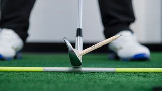 A golf club with a pencil attached to the face