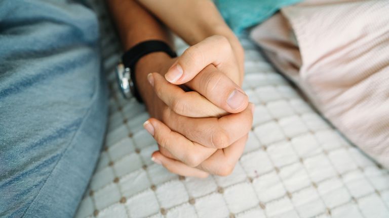 Two people holding hands sitting on a bed