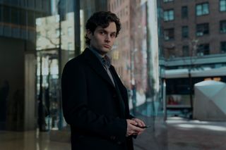 penn badgley as joe goldberg in a peacoat texting on his phone outside of a new york office building in a first look photo of season 5