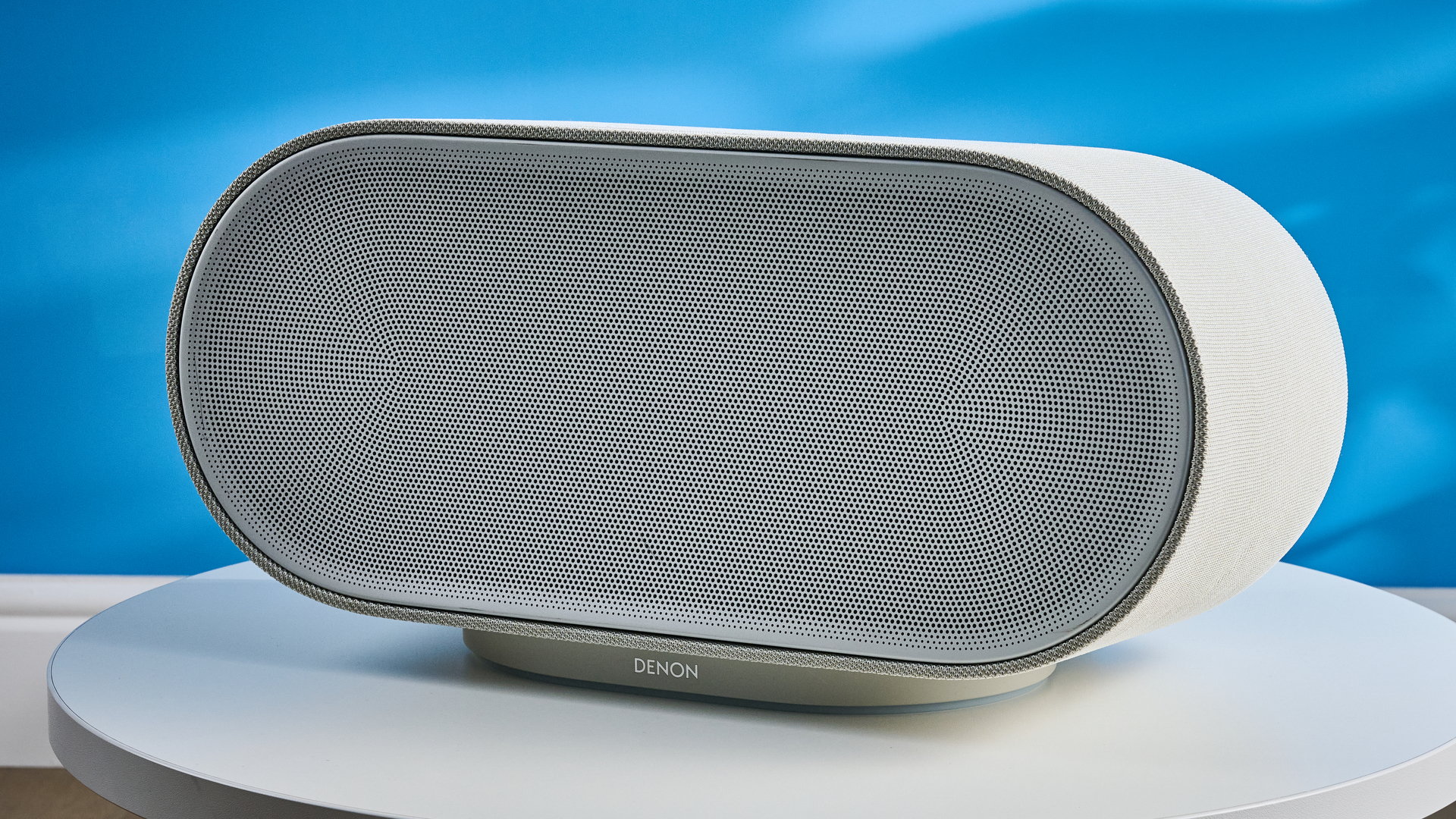 the denon home 600 home speaker in stone color photographed against the blue tom's guide background